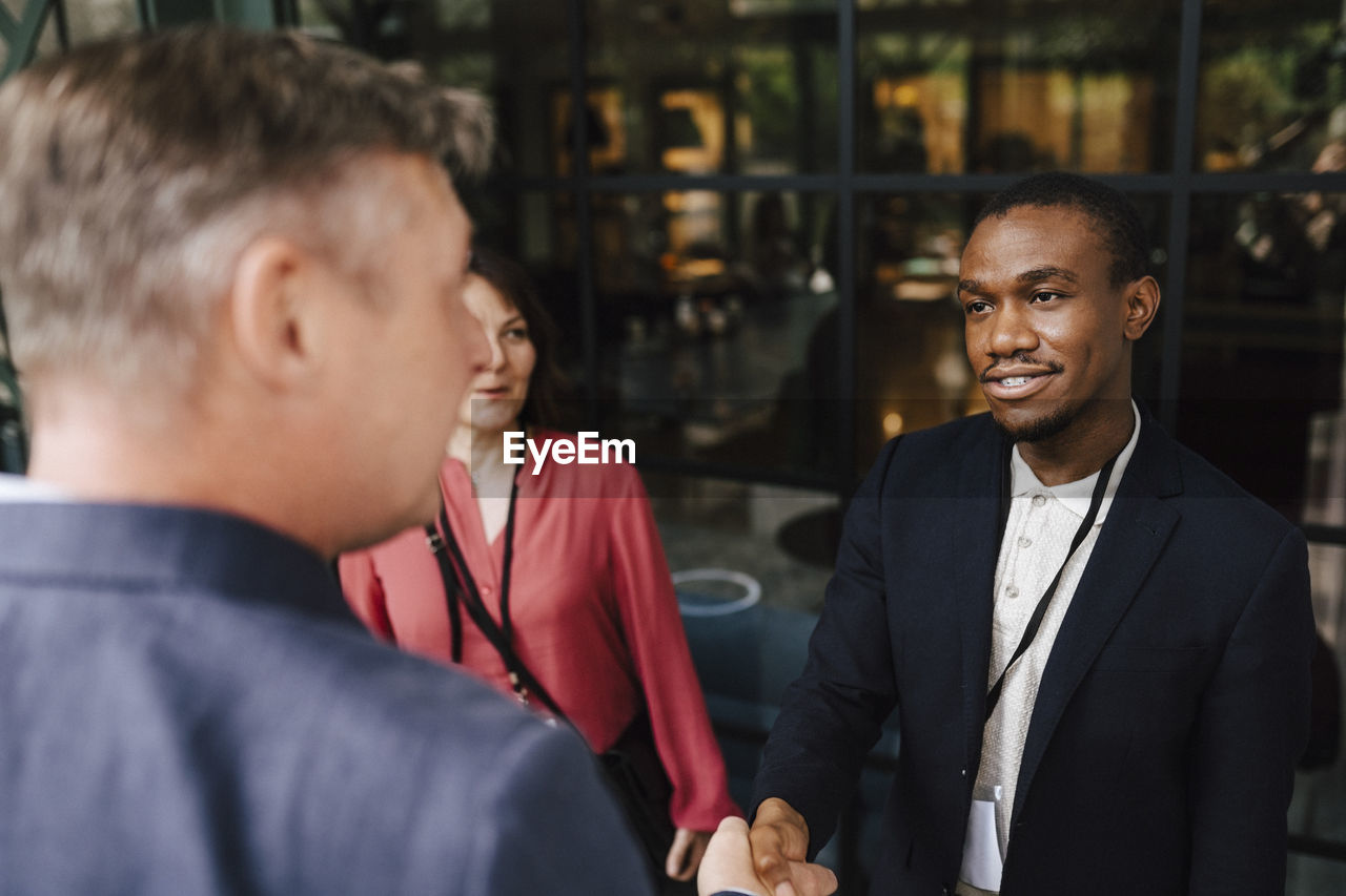 Male professional greeting mature businessman with handshake during seminar at convention center