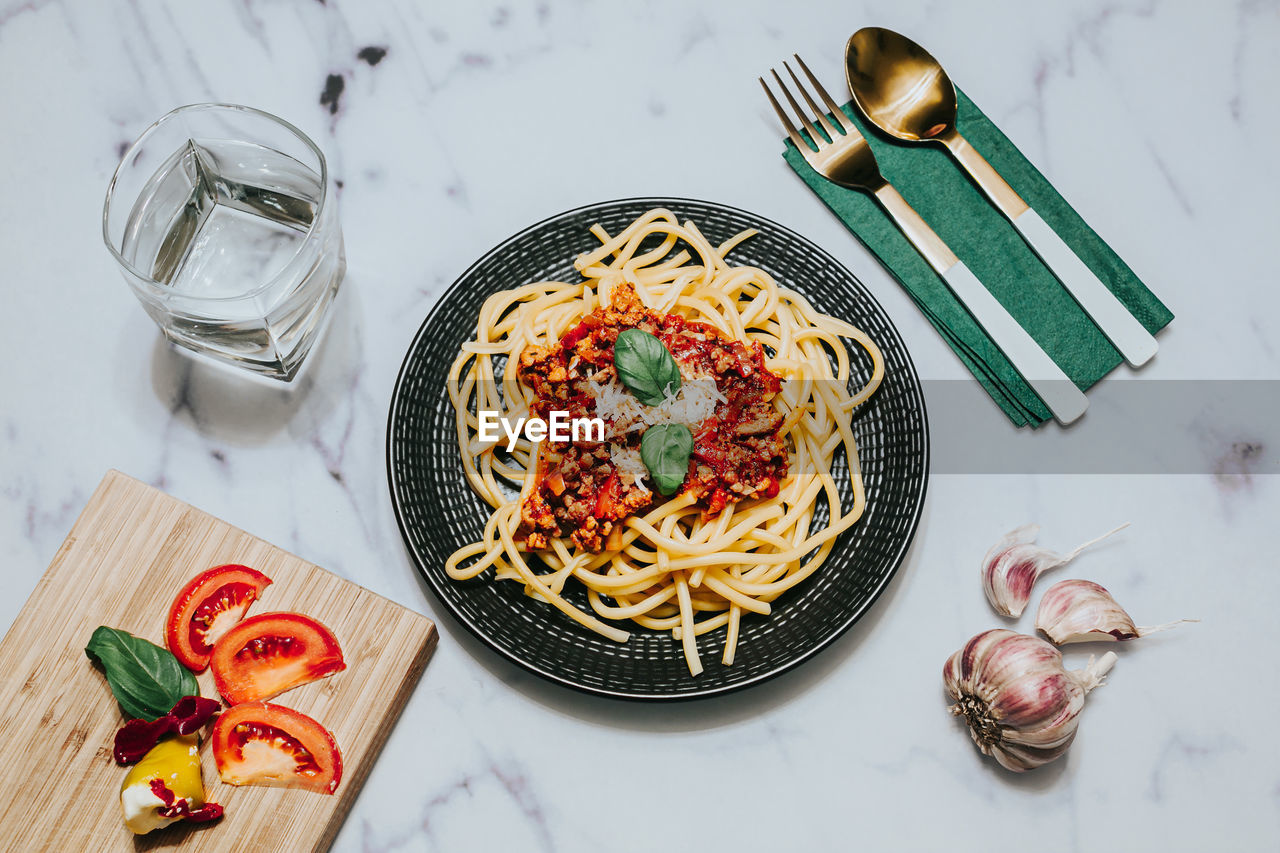 Top view of pasta with bolognese sauce on black plate with eateing utensil