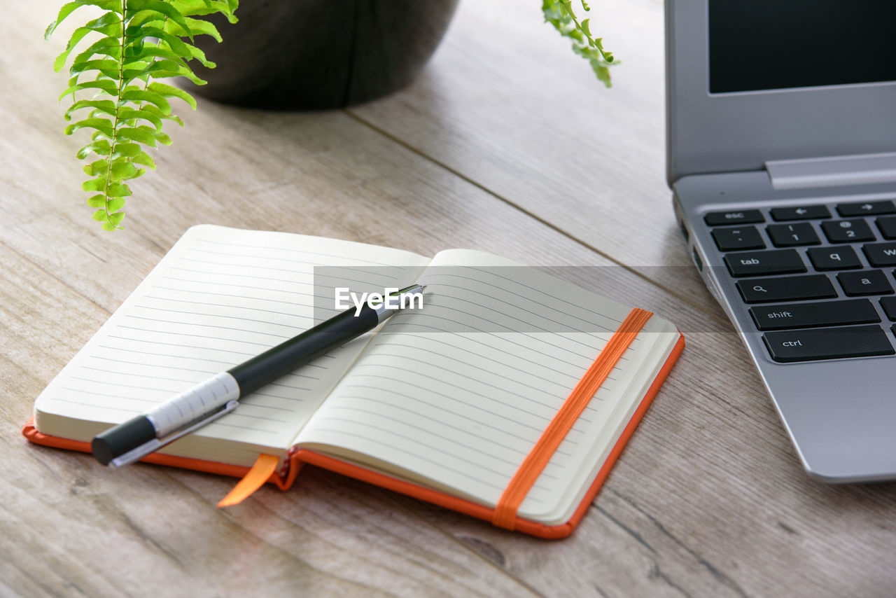 Close-up of pen on book by laptop at table