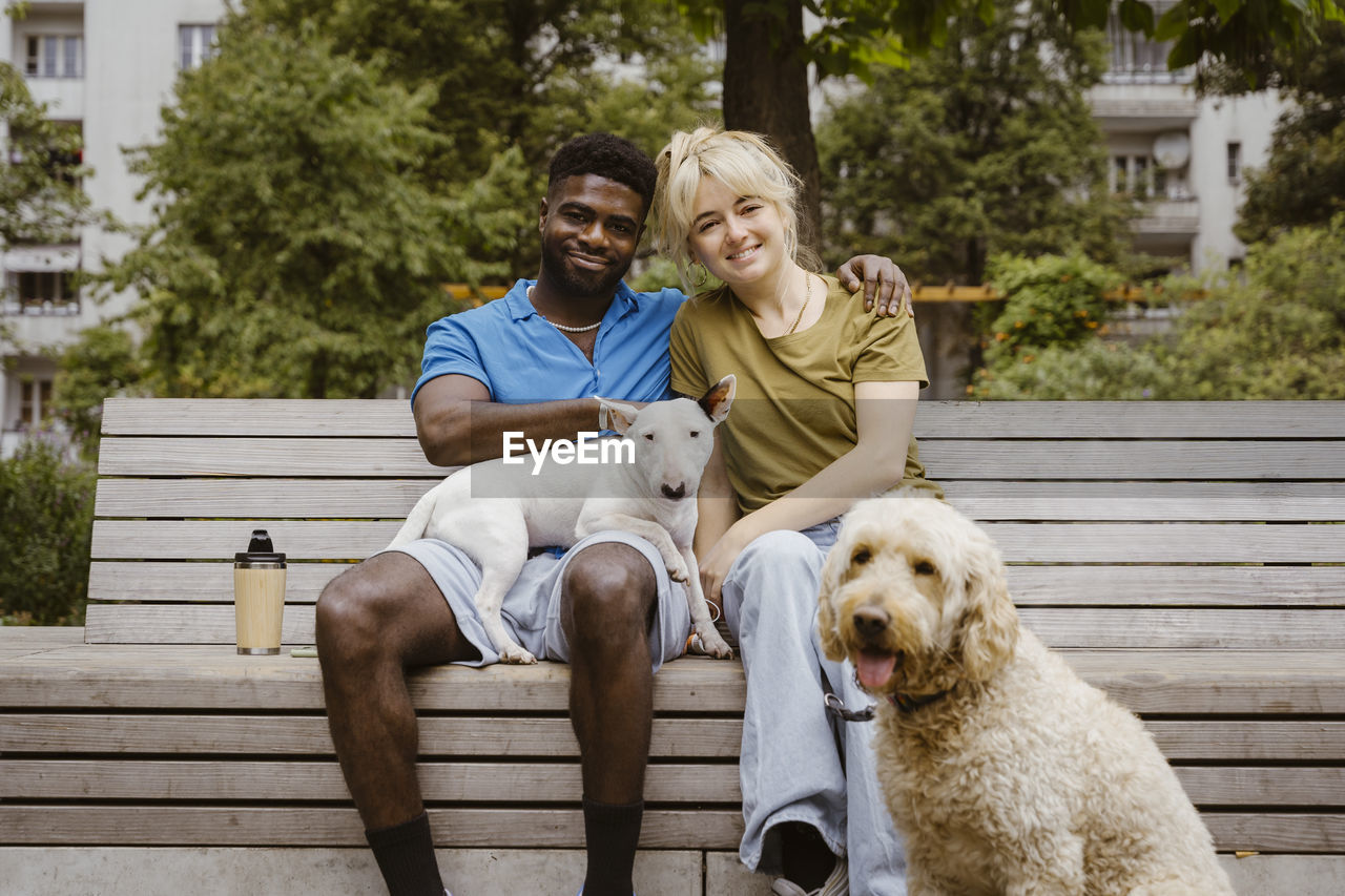 Portrait of smiling heterosexual couple with dogs in public park