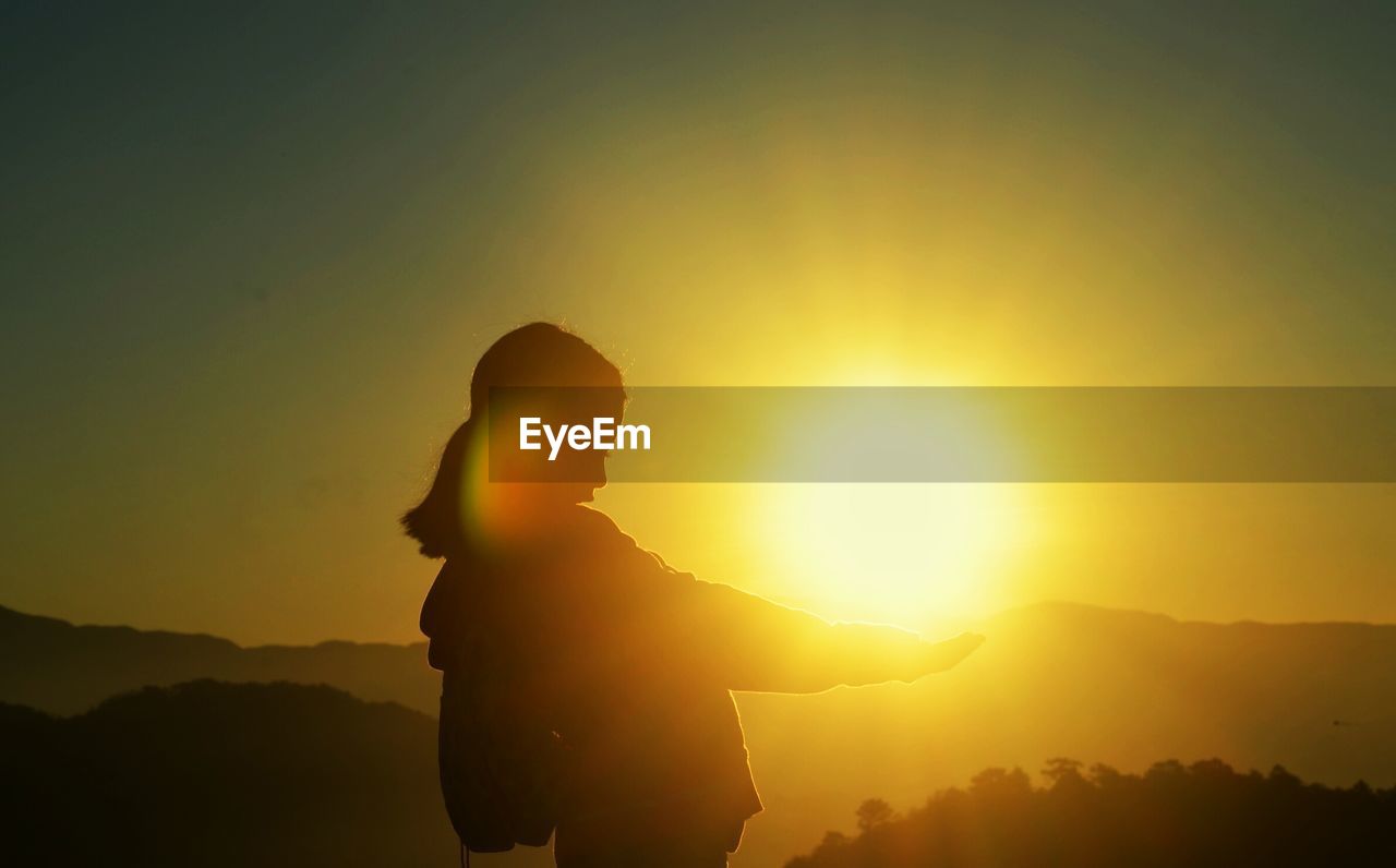 Optical illusion of silhouette woman holding sun against clear sky