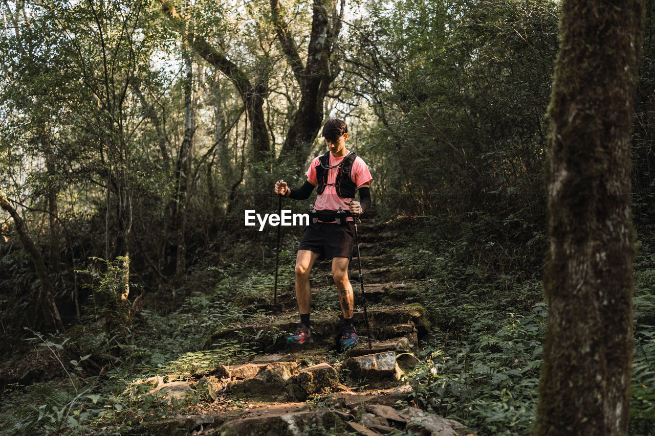 Man traveler with trekking poles walking up old stone stairs in jungles