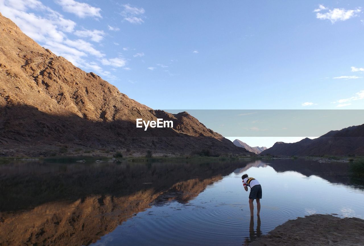 Rear view of man in lake with mountain reflection against sky