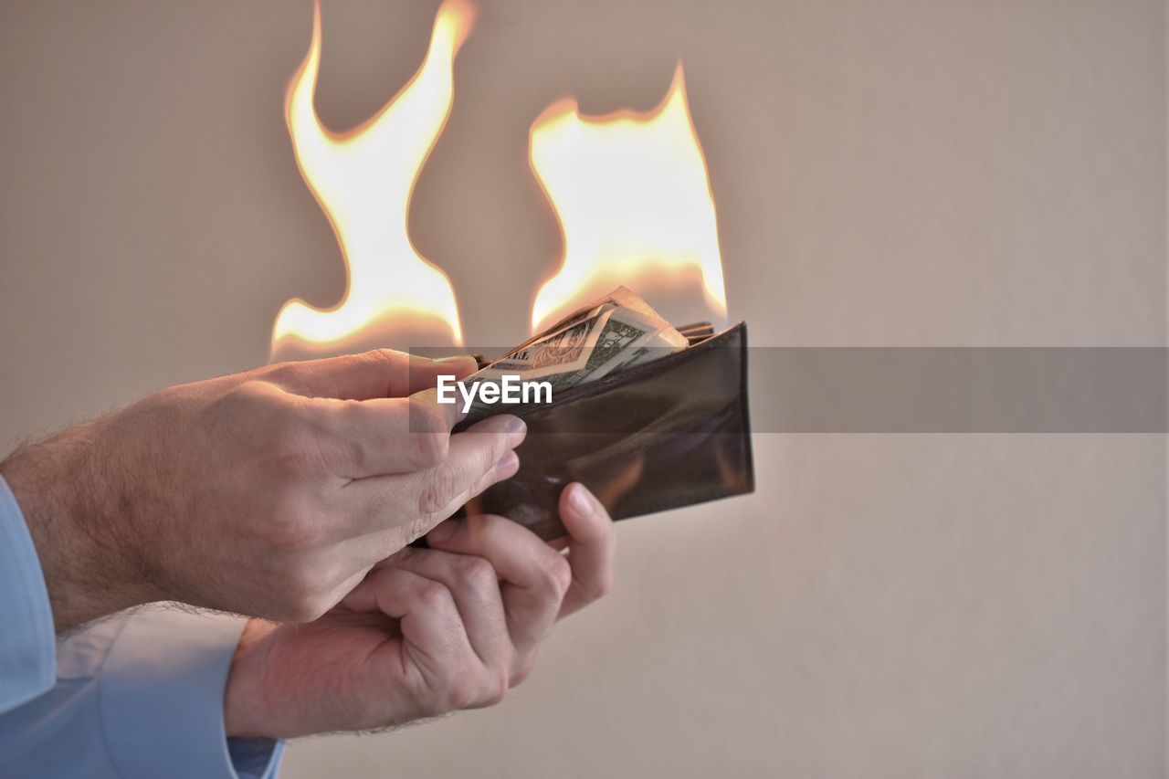 Cropped hands of man removing burning paper currencies from wallet