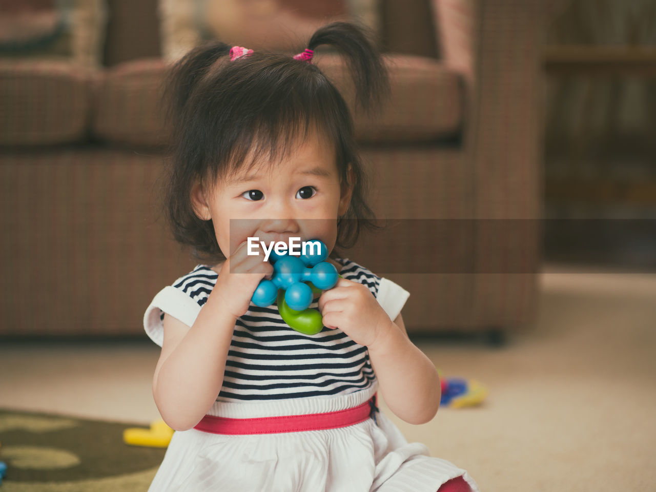 Cute girl biting toy while sitting at home