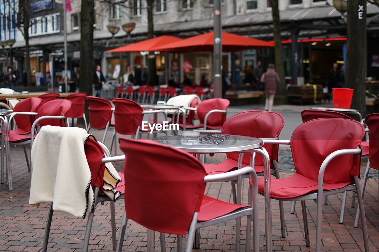 Empty chairs and tables at sidewalk cafe against buildings in city