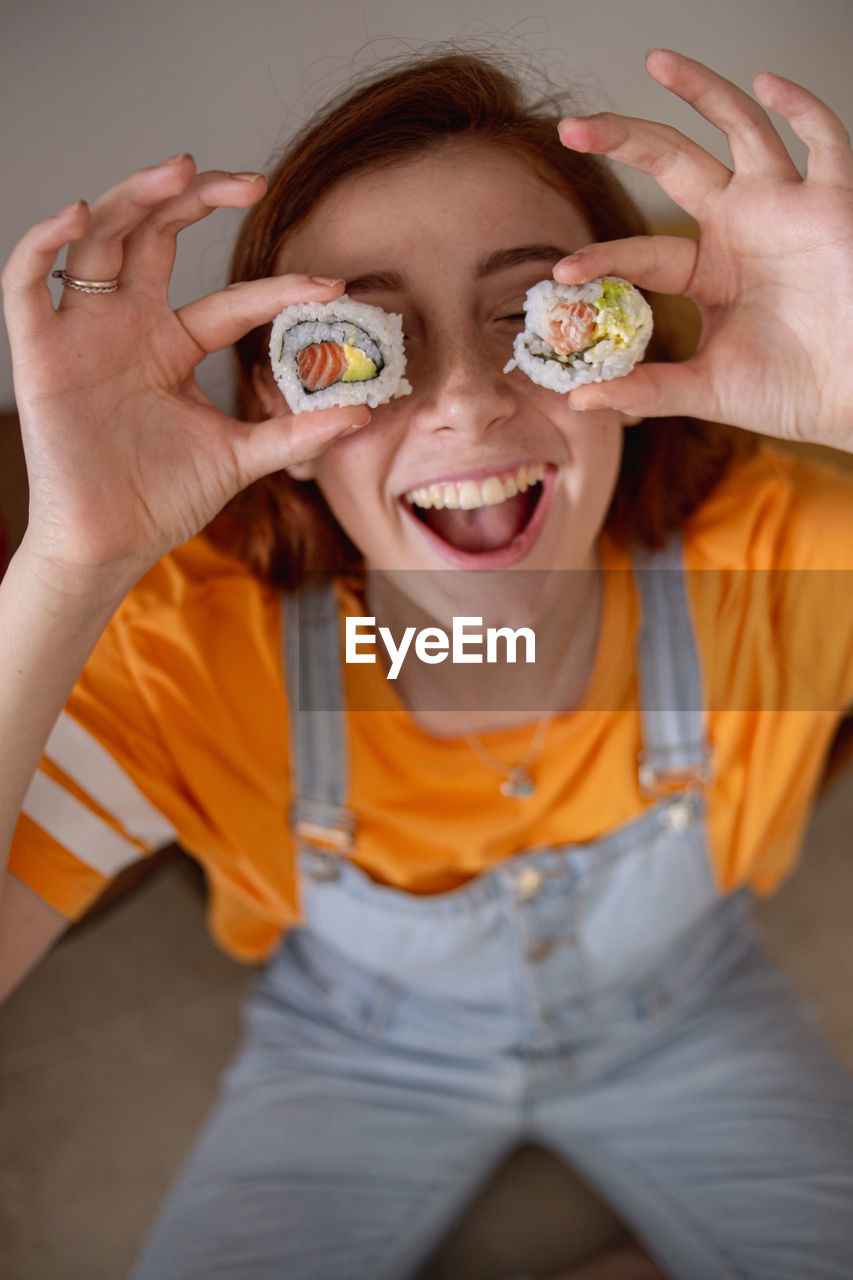 From above delighted young female keeping tasty sushi near eyes while having lunch at home