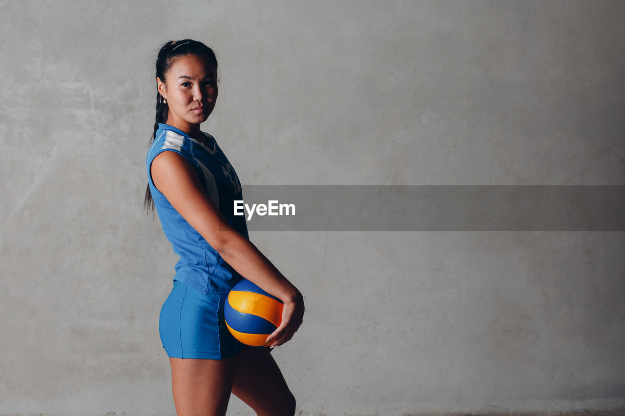 Portrait of young woman holding ball against wall