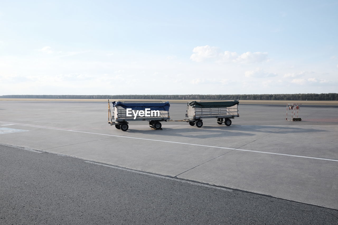 Luggage carts at airport runway against sky