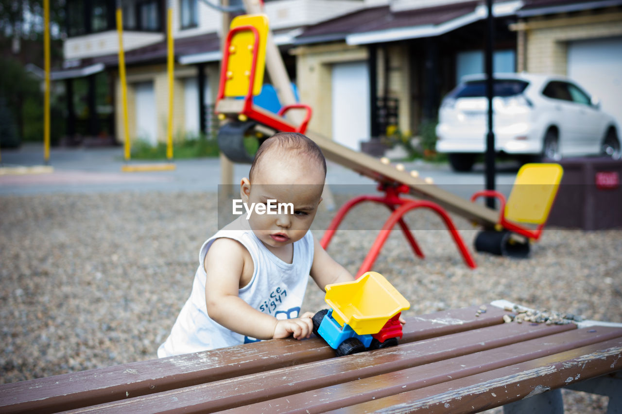 Cute pretty little baby baby plays with toy car on children playground
