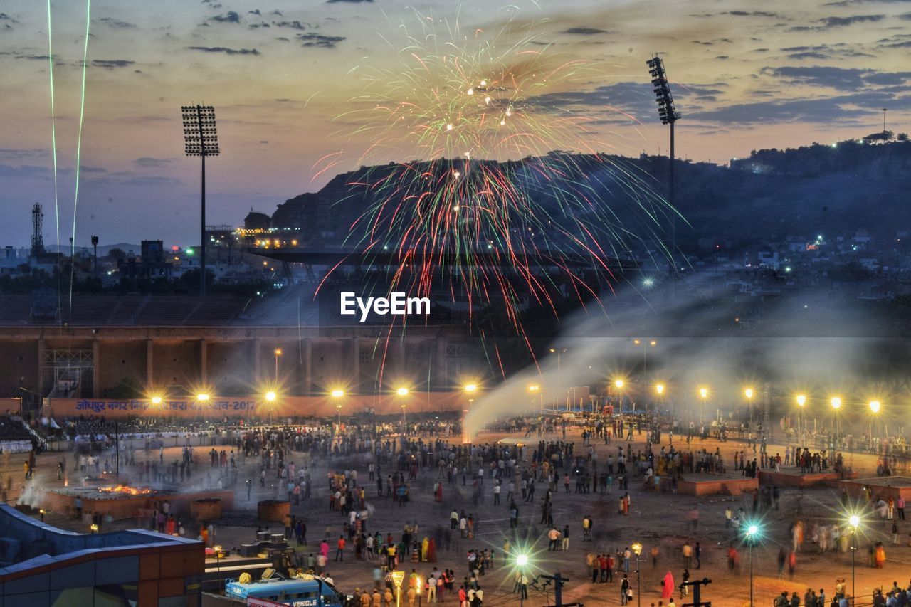 Firework exploding over crowd at town square in city during sunset