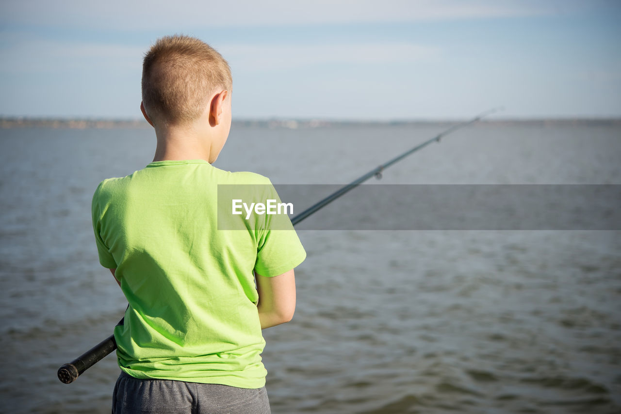 REAR VIEW OF BOY LOOKING AT SEA SHORE