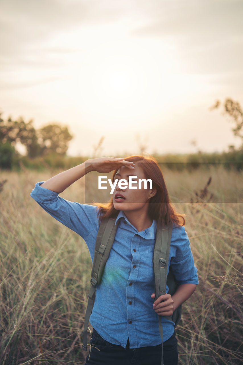 Beautiful young woman standing on field against sky