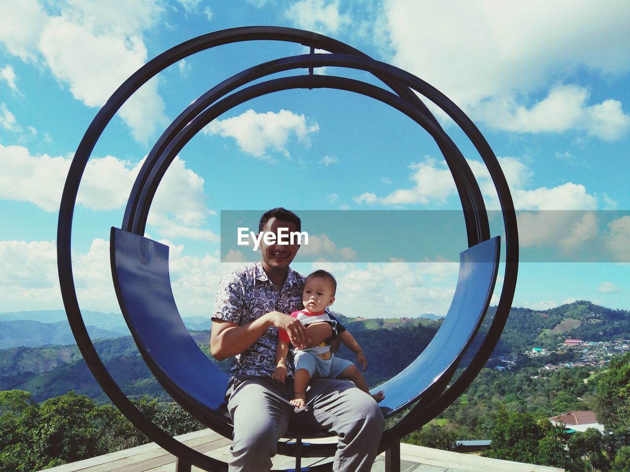 Portrait of father sitting with son against sky