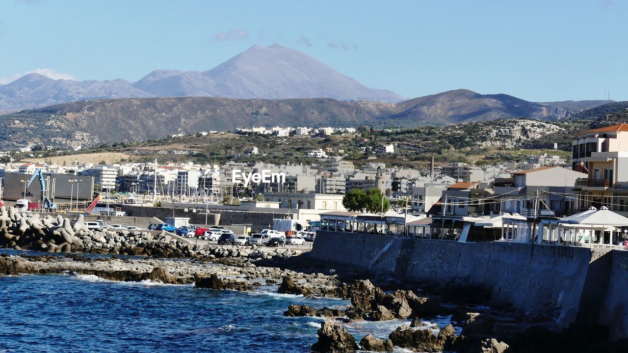 Town by sea and mountains against sky