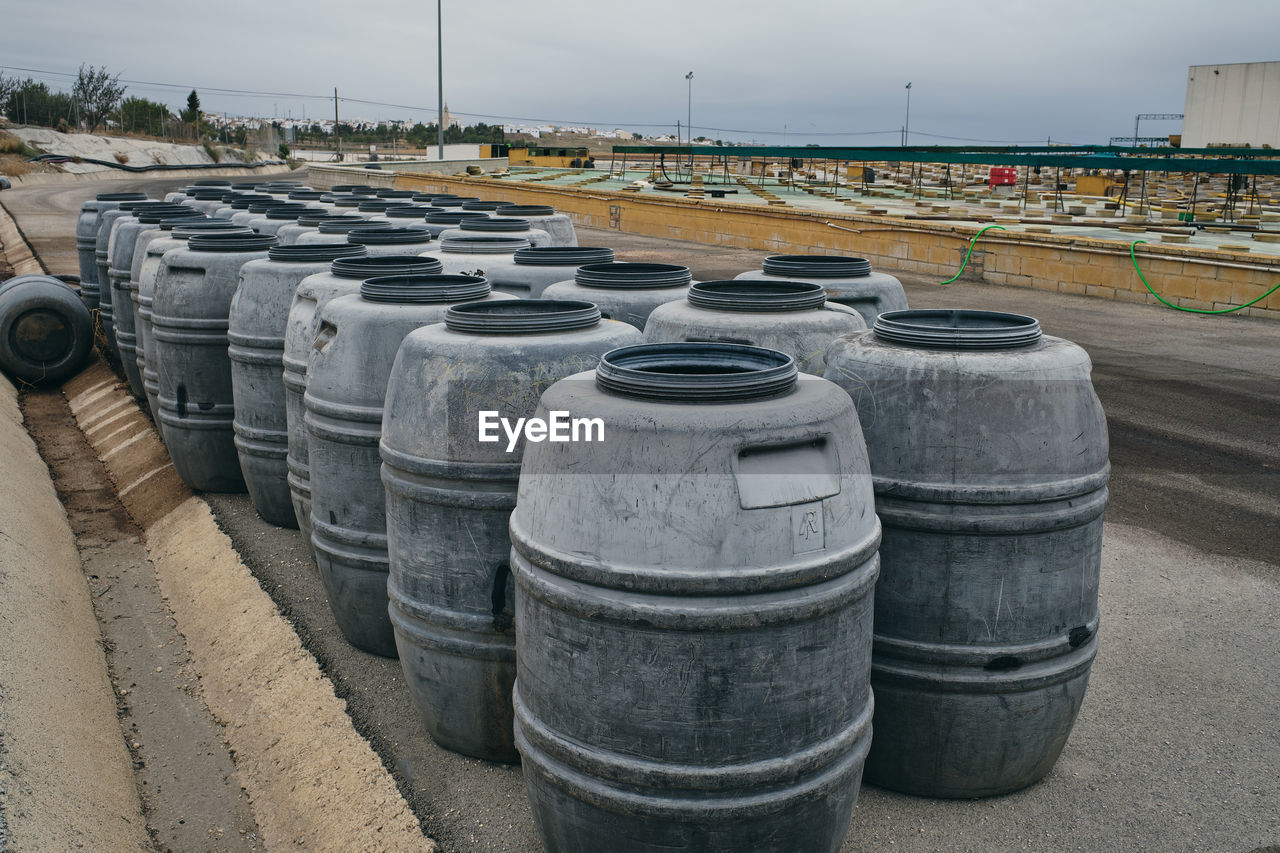 Rows of shabby metal barrels placed in shabby industrial place of factory on cloudy day
