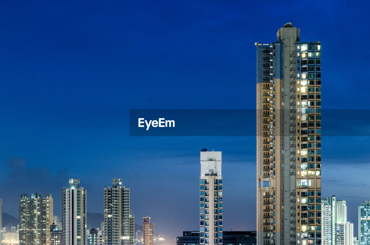 Illuminated skyscrapers against blue sky at night