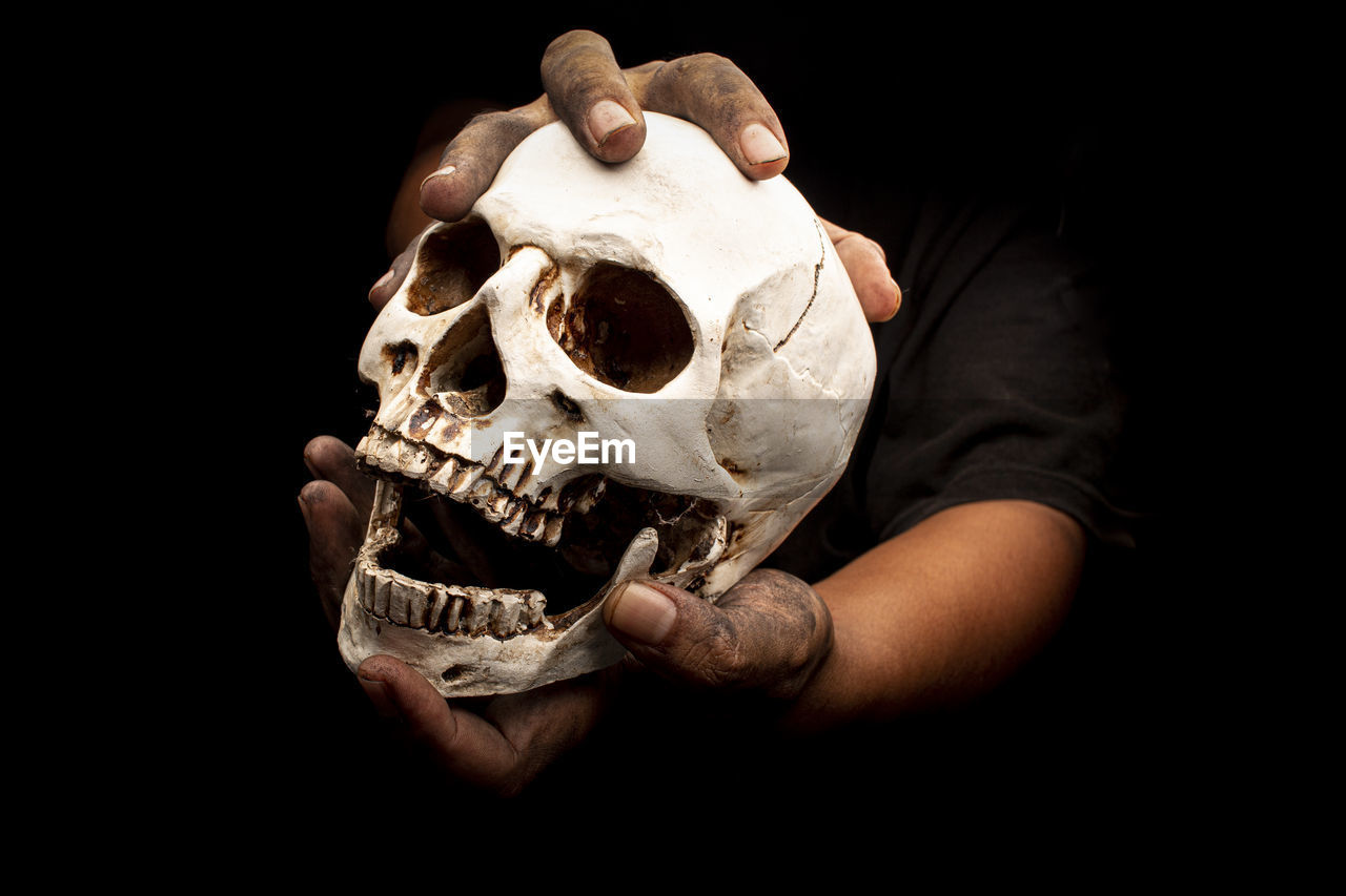 Cropped image of hand holding skull against black background