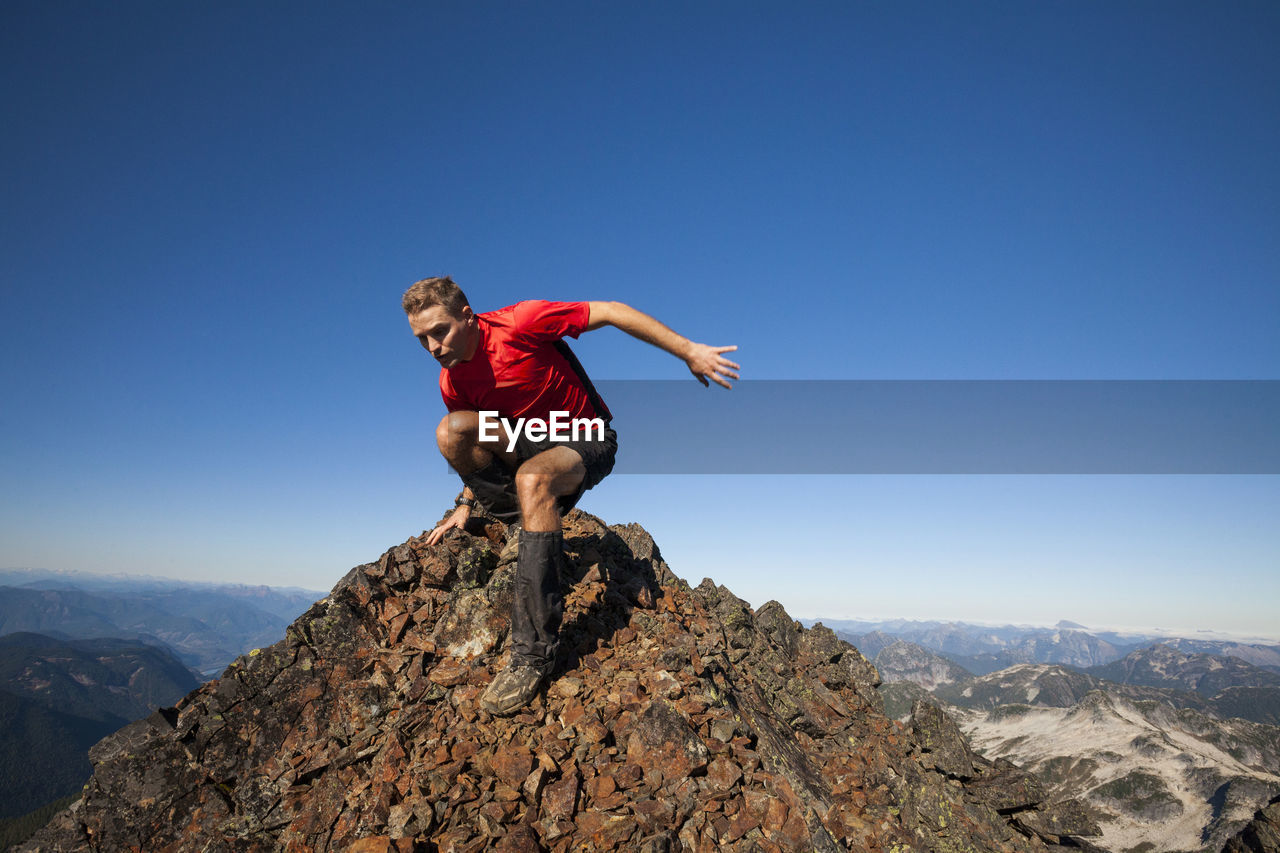 Man moving down from rocky mountain against clear blue sky during sunny day