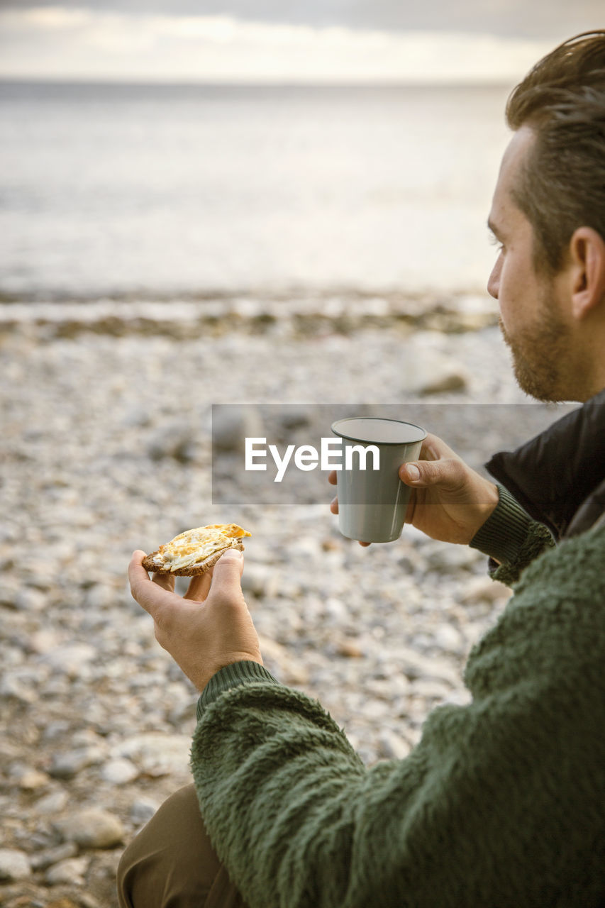 Cropped image of man eating snack with coffee at beach