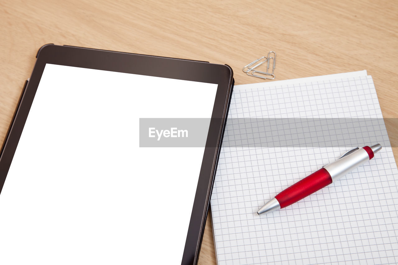 High angle view of digital tablet and blank notepad on table