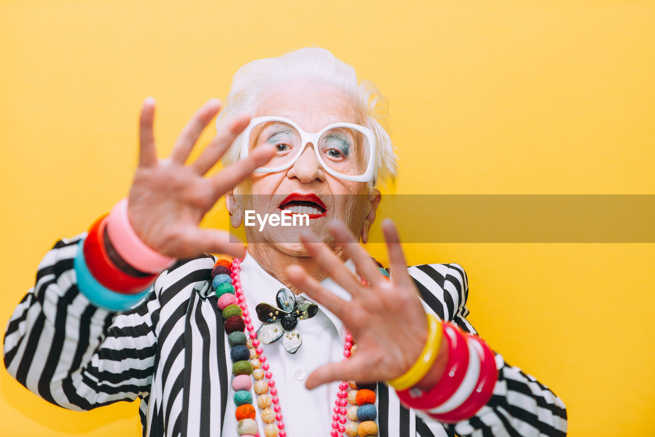 Portrait of senior woman gesturing against yellow background