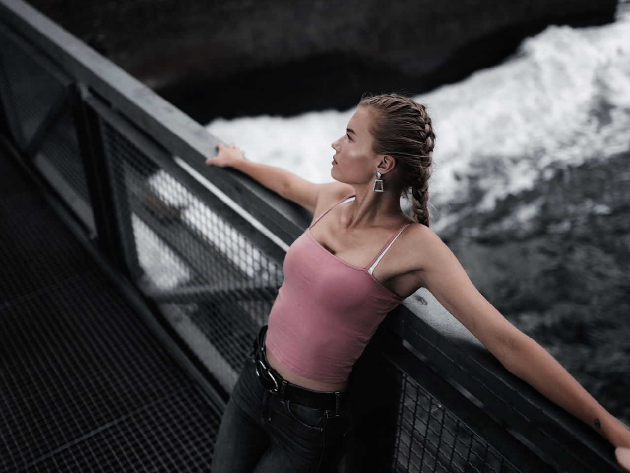 Side view of young woman standing against railing above river 