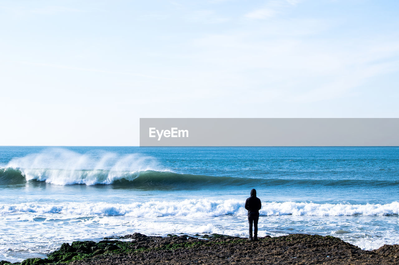 Rear view of man standing at sea shore against sky