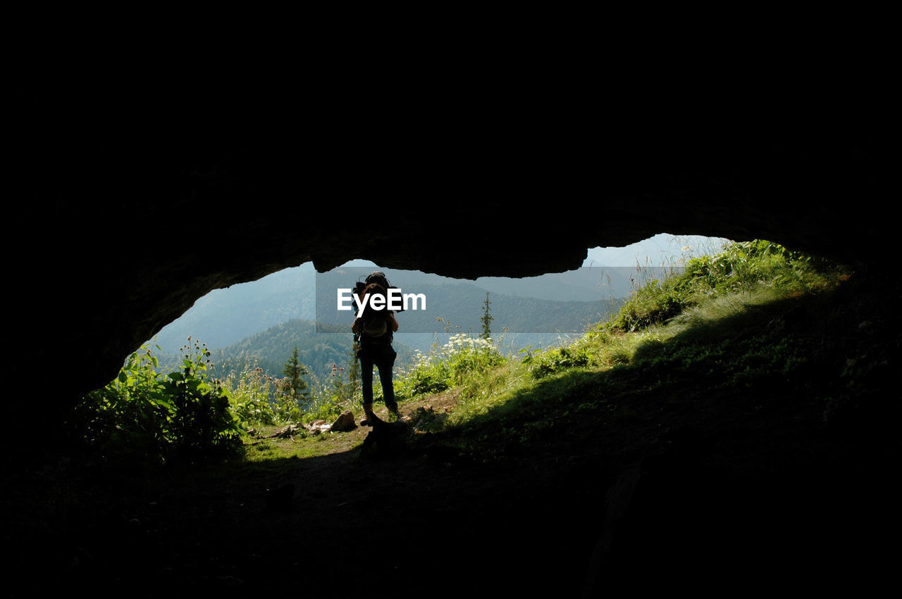 cave, darkness, one person, silhouette, full length, leisure activity, activity, nature, adventure, adult, hiking, lifestyles, men, standing, exploration, mountain, travel, rock, land, holiday, vacation, beauty in nature, trip, outdoors, sky, copy space, walking, dark, scenics - nature, tranquility, plant, non-urban scene, landscape, light, reflection, night, travel destinations, environment, tree, solitude, tourism, sports
