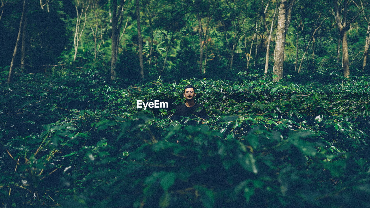 Young man with closed eyes standing amidst plants