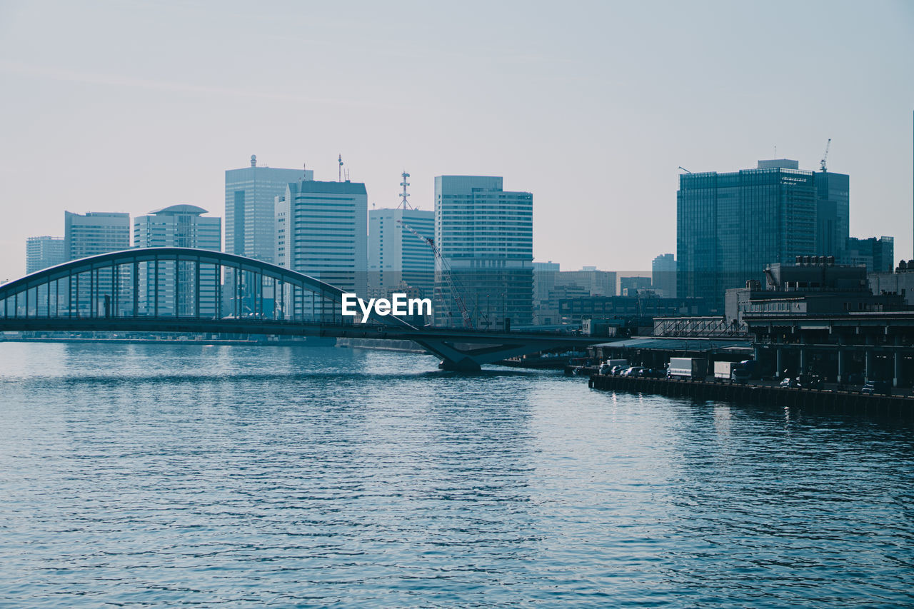 BRIDGE OVER RIVER AND BUILDINGS AGAINST CLEAR SKY