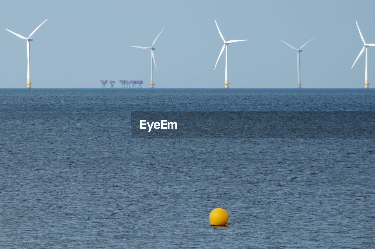 Wind turbines by sea against sky