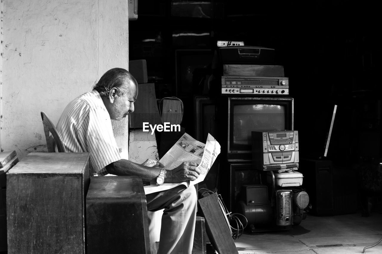 Man reading newspaper while sitting outside shop