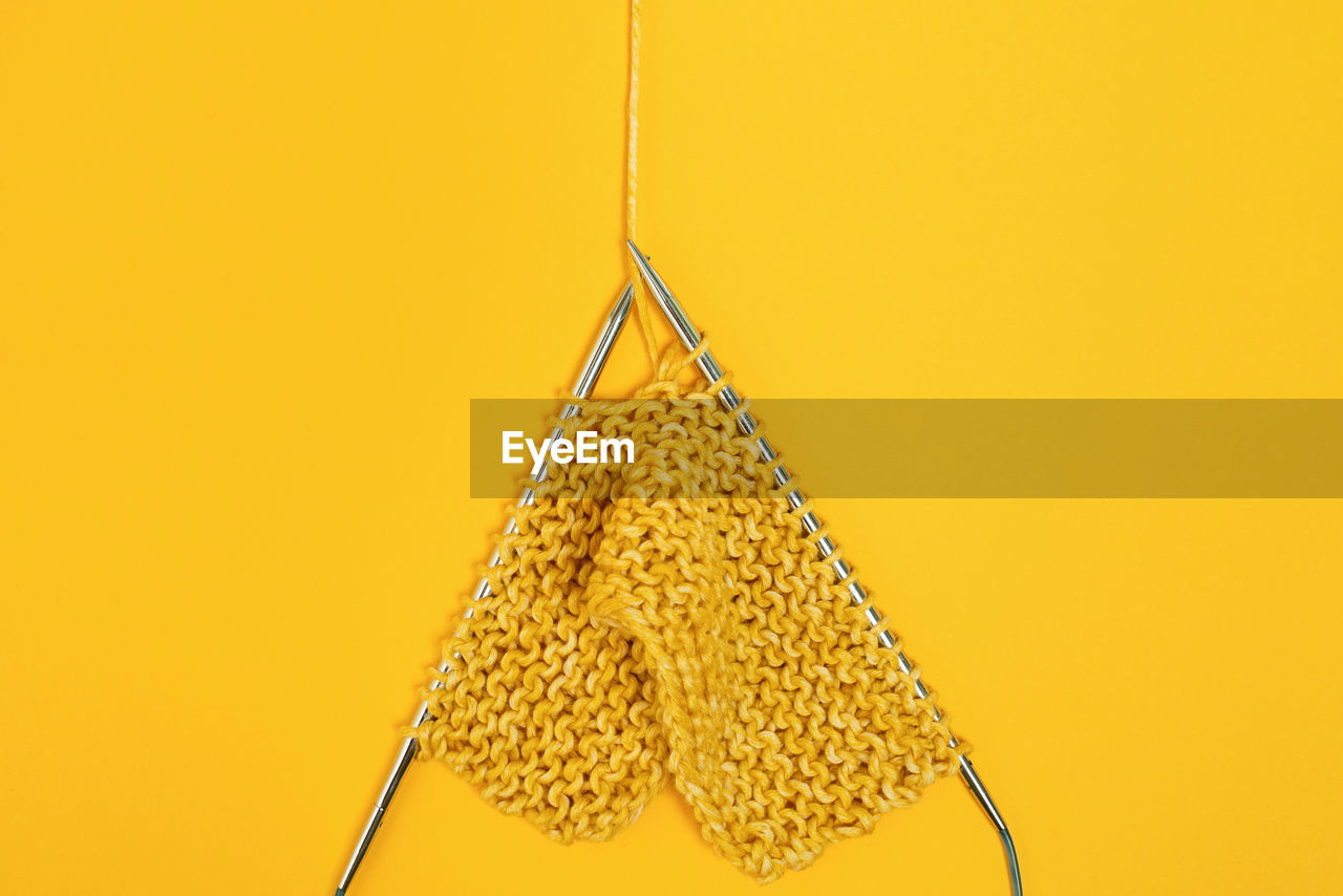 From above of knitting needles with yarn against yellow background