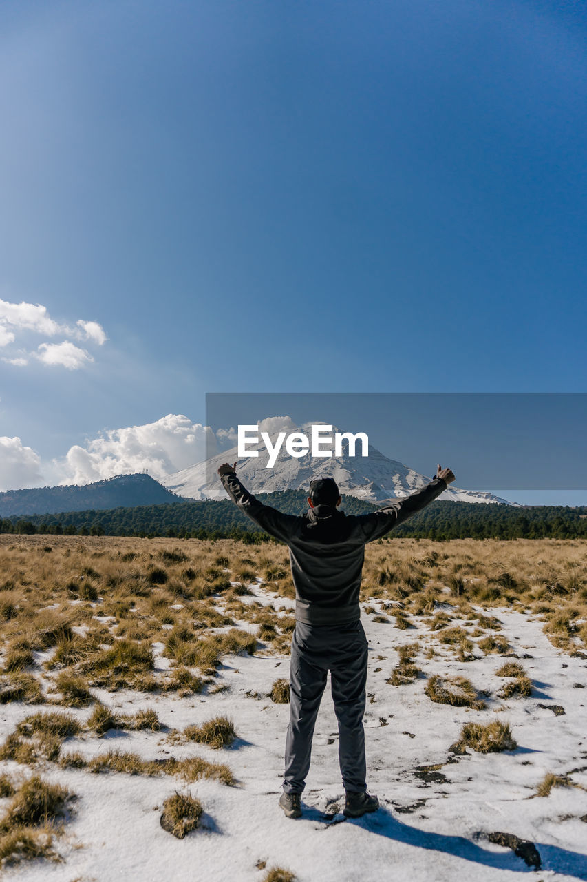 Rear view of man standing on snowcapped mountain against clear blue sky