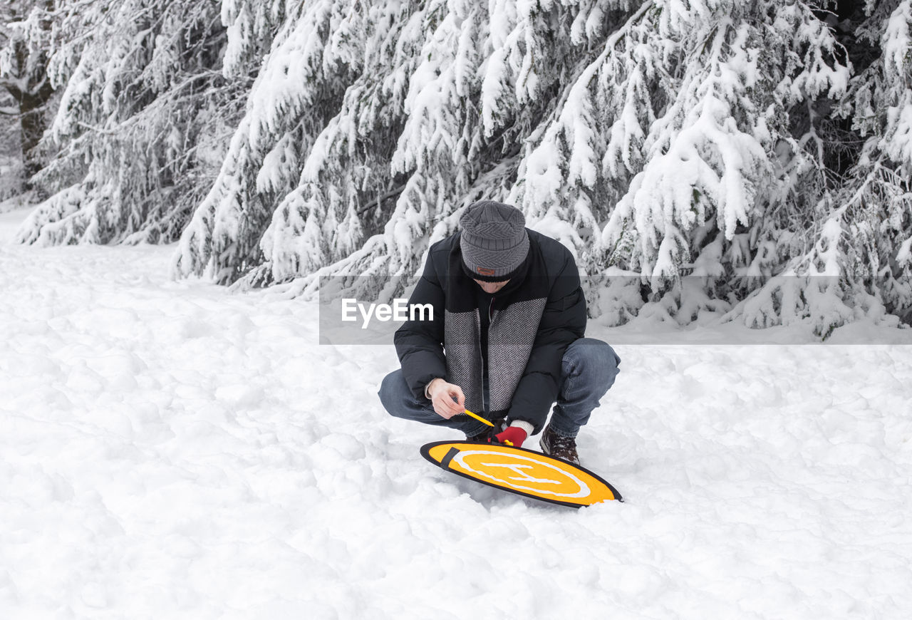 A young man sets up a platform for a drone in a winter forest.