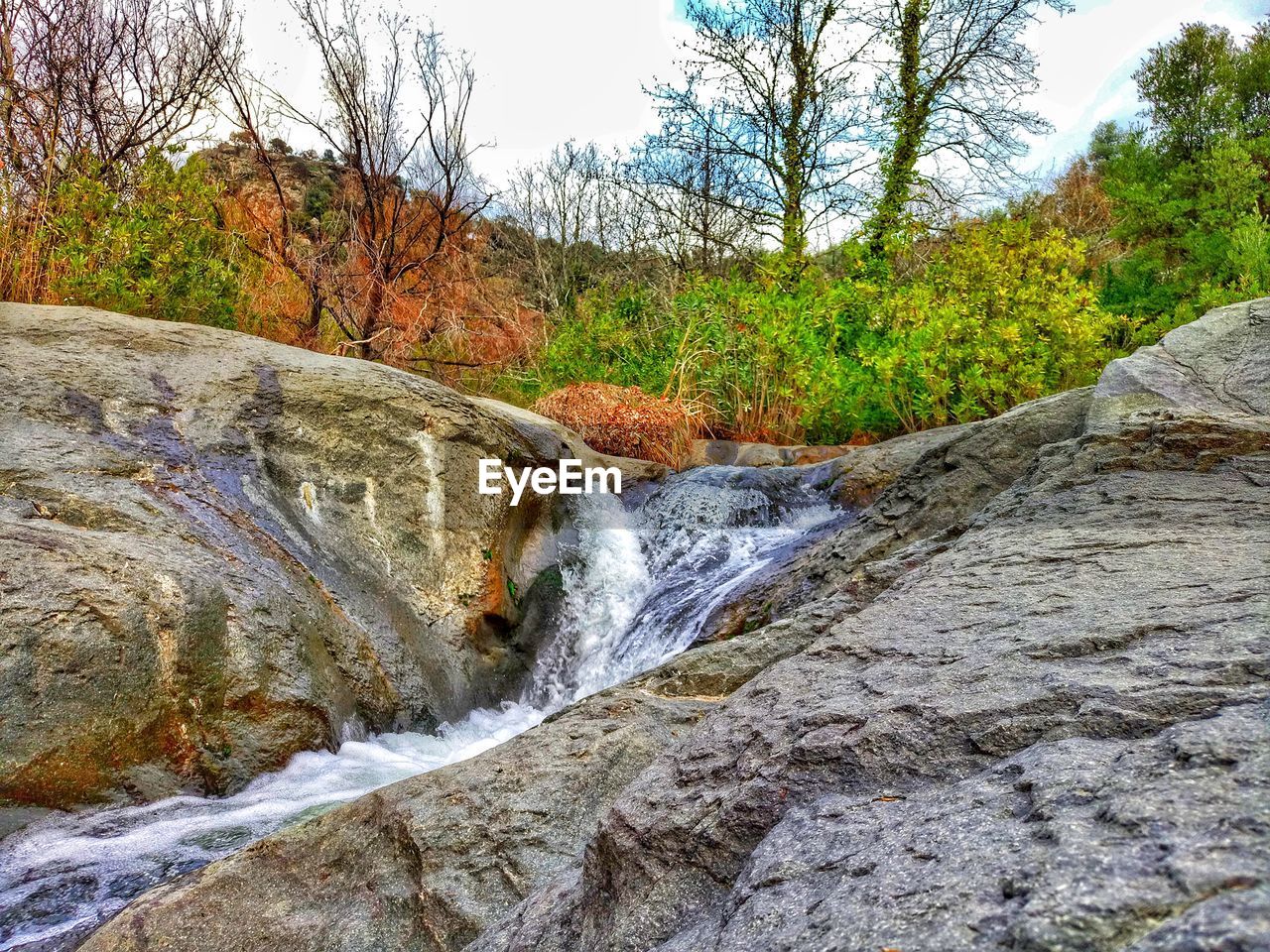 SCENIC VIEW OF WATERFALL IN FOREST AGAINST SKY