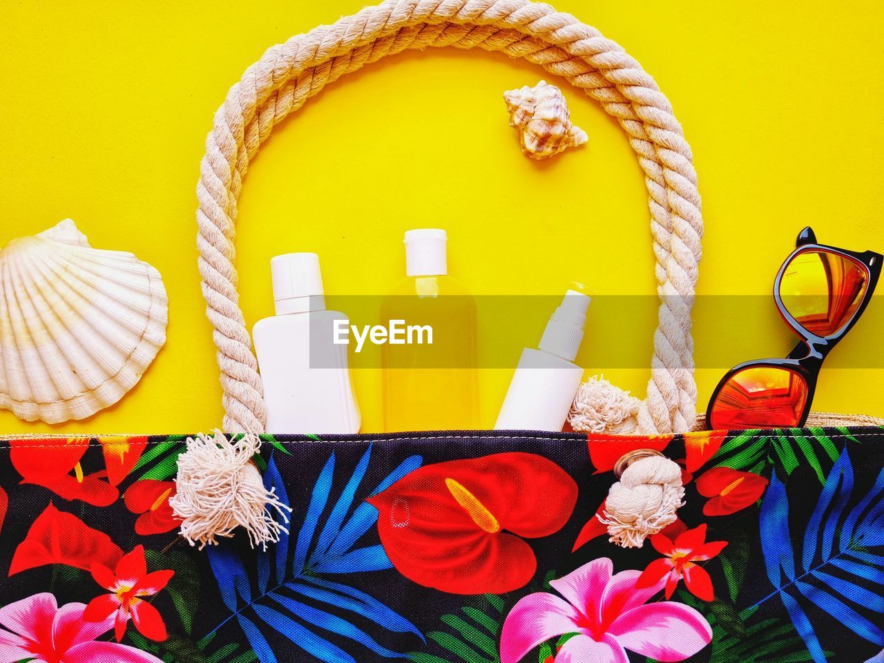 Colorful beach bag with sunscreen and sunglasses on yellow background