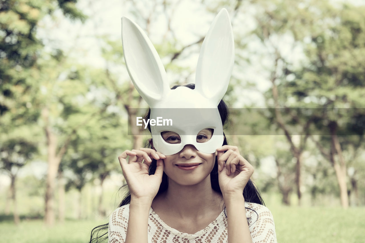 Portrait of young woman wearing mask while standing against trees at park