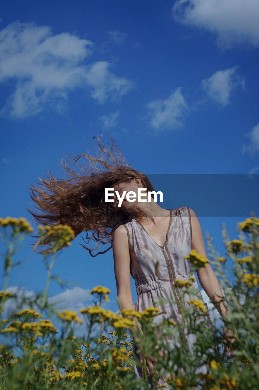 Low angle view of woman tossing hair while standing at field