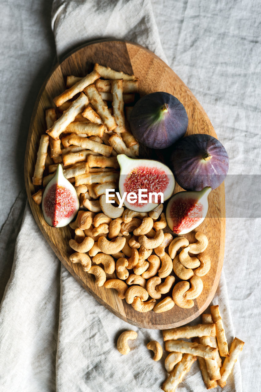 Wine appetizers namely ripe figs, cashews, and salty bread sticks on the table indoors.