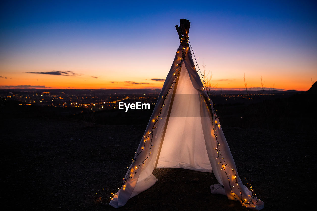 Illuminated tent on field against sky at sunset