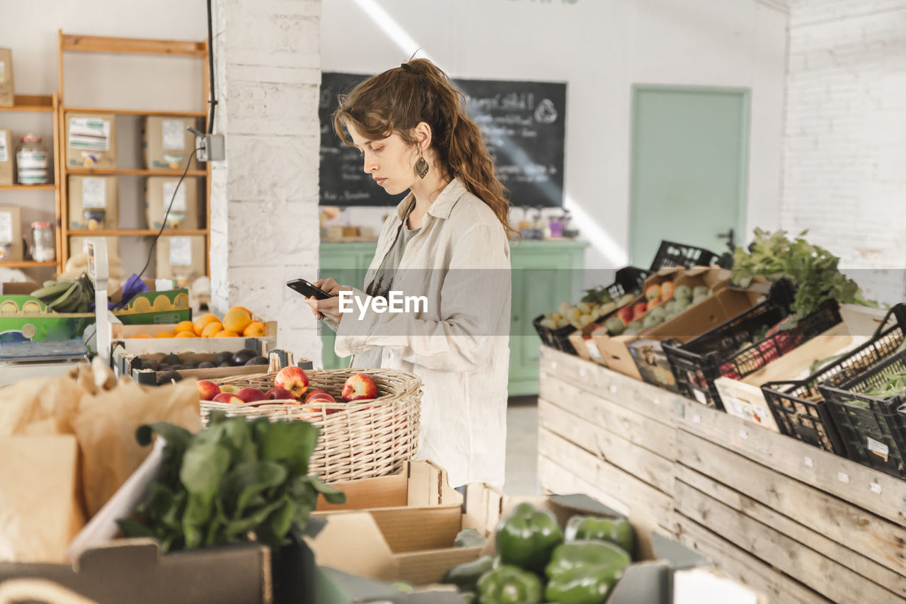 Customer using smart phone standing in vegetable store
