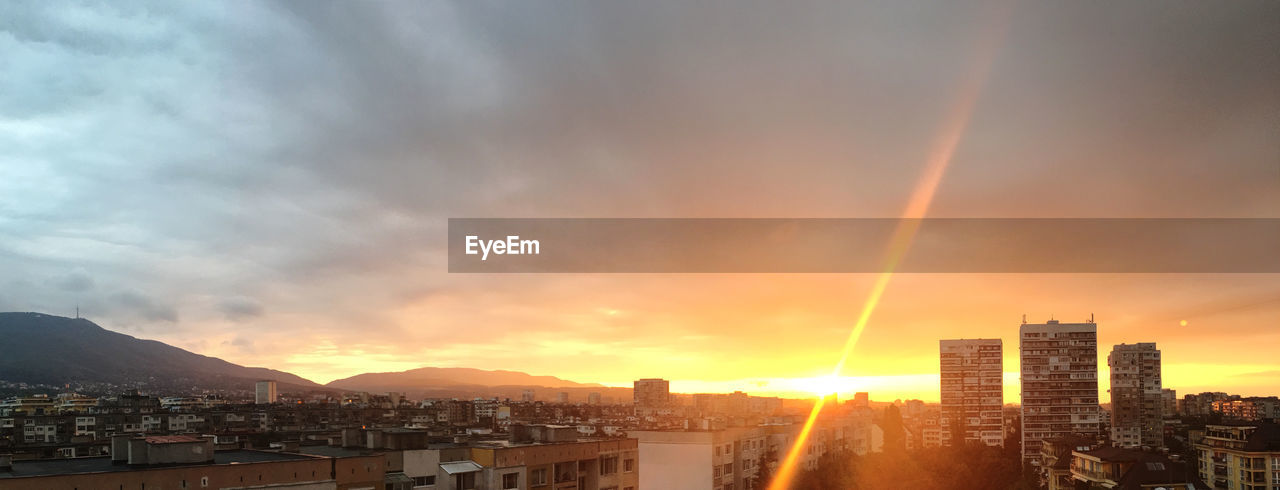 LOW ANGLE VIEW OF SUNLIGHT STREAMING THROUGH CLOUDS OVER CITY