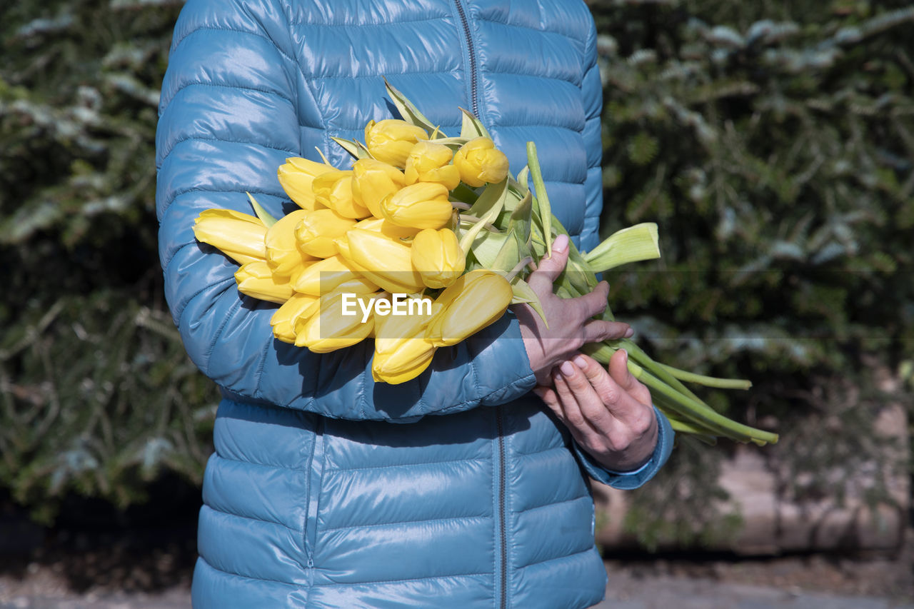 Woman in a blue jacket with a bouquet of yellow spring tulips, mother's day gift