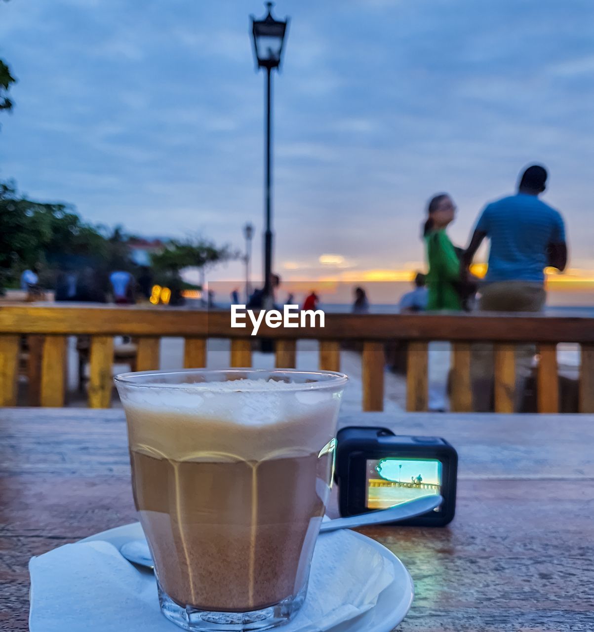 Close-up of coffee cup while couple standing in background against sky
