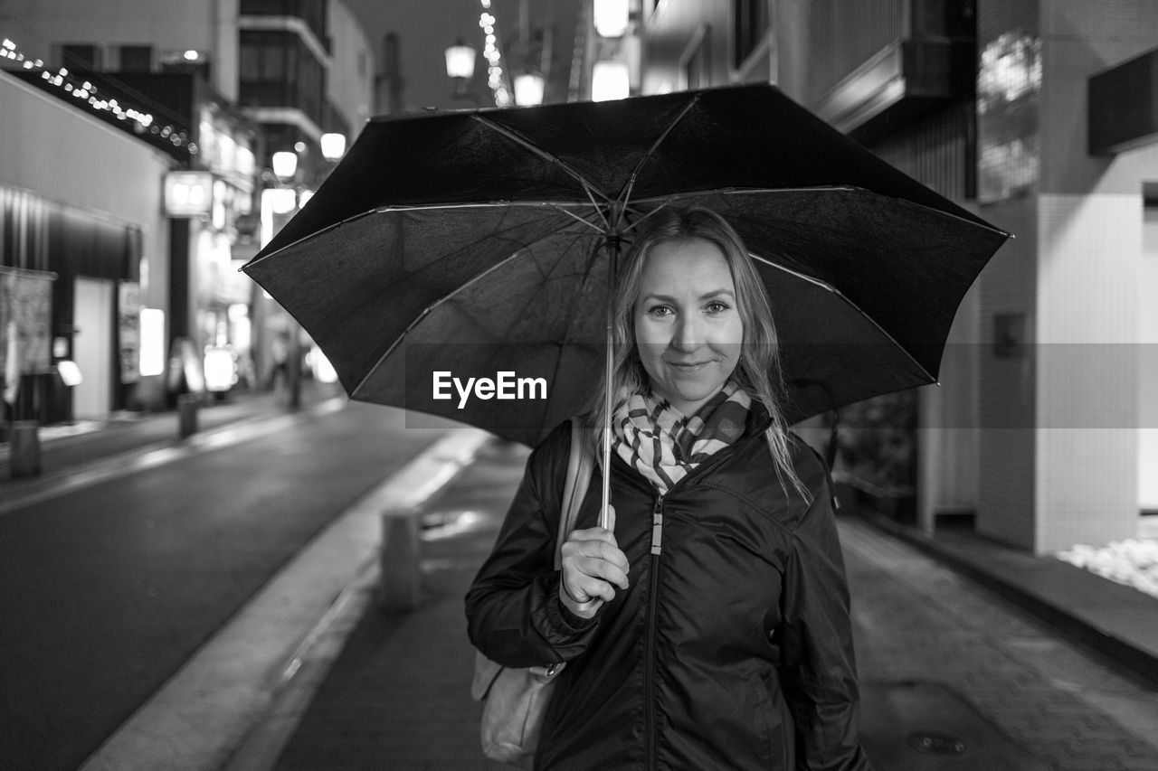 Portrait of smiling woman holding umbrella at night during rainy season