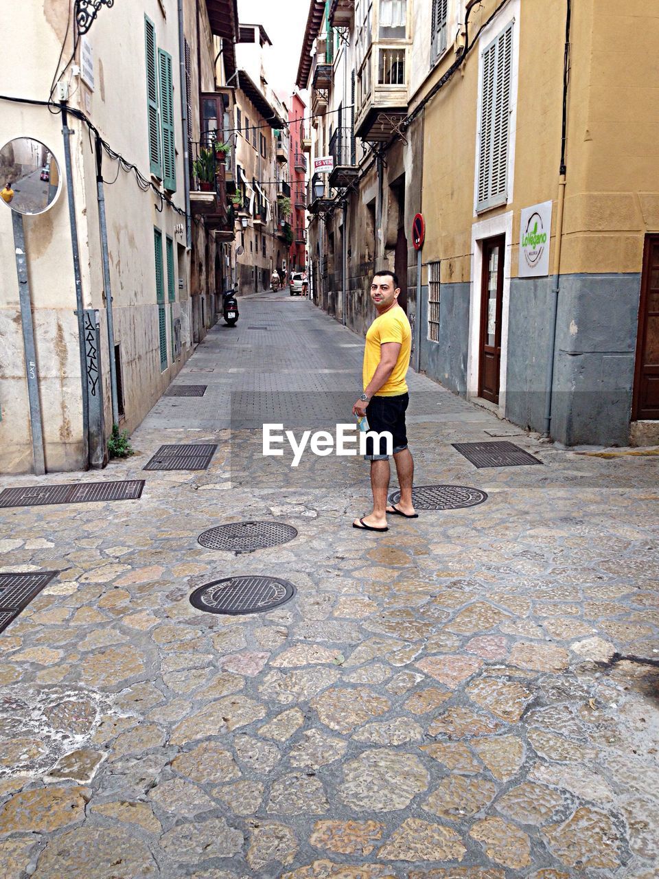 Portrait of man standing on alley by buildings in city