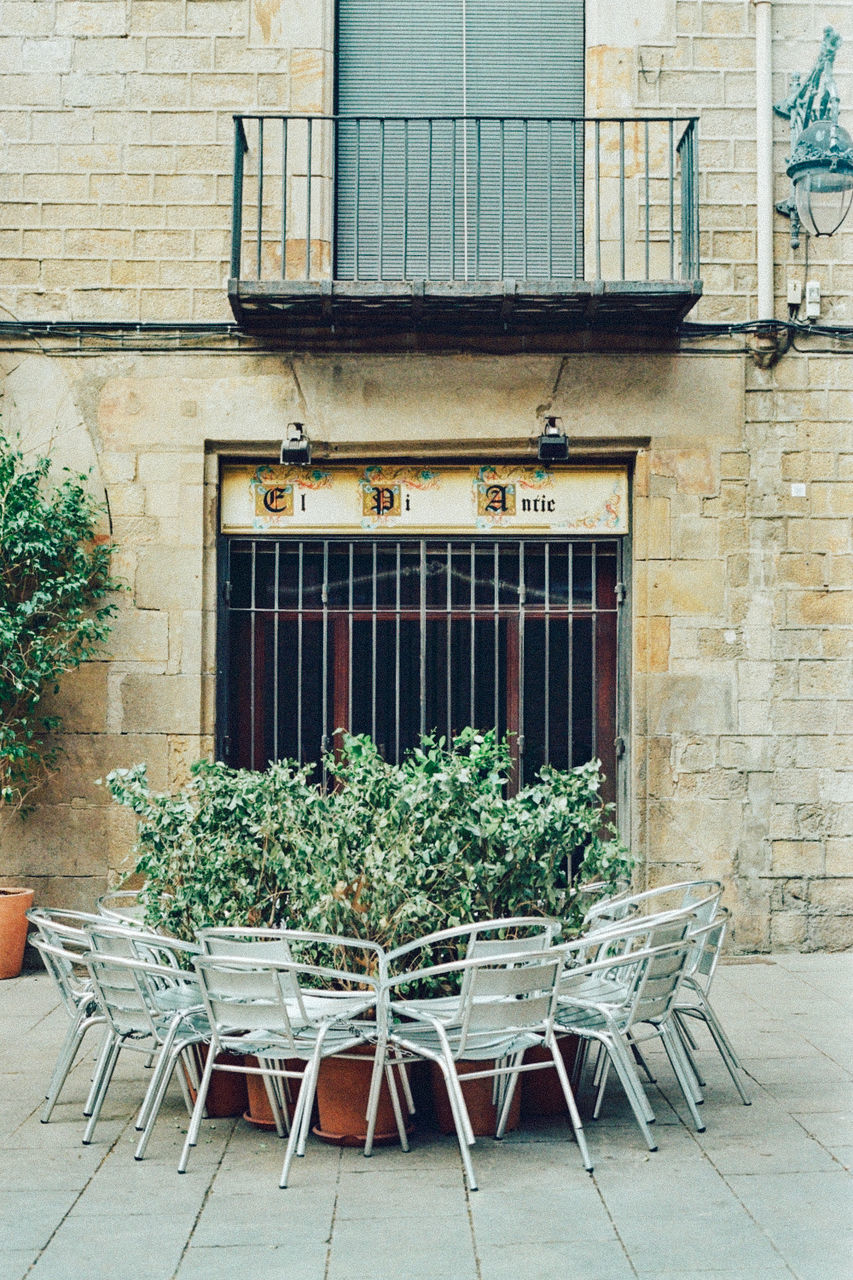 Empty chairs by potted plants against building