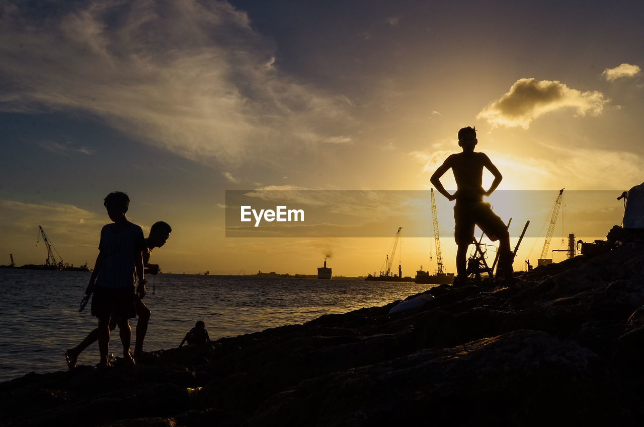 Silhouette men standing on beach against sky during sunset